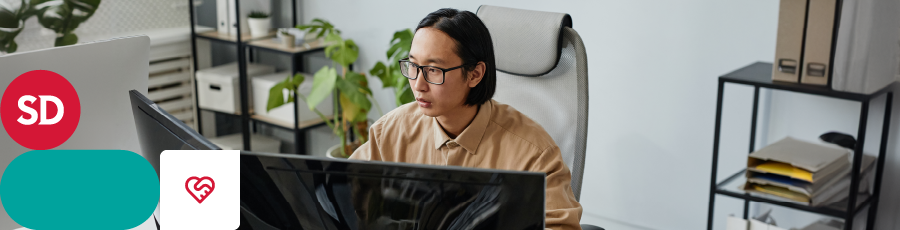 Person working at a desk with multiple monitors, shelves with books and plants, and office logos.

