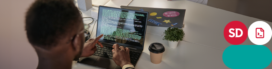 Person working on a laptop with code displayed on the screen, coffee cup and potted plant on desk.

