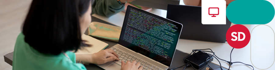 Person coding on a laptop at a desk with multiple laptops and office supplies.

