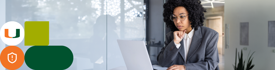 "Person working on a laptop at a desk, with a glass wall and office decor in the background."